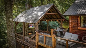 A wooden deck with a stone fireplace, a grill, and a seating area. - Four Seasons Mountain Escape - Riverfront | Pet Friendly | Hot Tub (Blue Ridge)