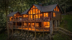 A multi-level wooden cabin with a balcony, stone foundation, and a hot tub. - Four Seasons Mountain Escape - Riverfront | Pet Friendly | Hot Tub (Blue Ridge)