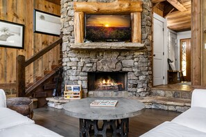 A cozy interior with a stone fireplace, a round table with a tray, and a staircase. - Four Seasons Mountain Escape - Riverfront | Pet Friendly | Hot Tub (Blue Ridge)