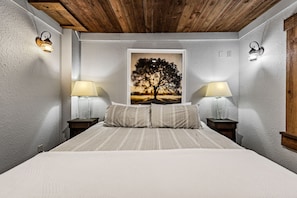 A bedroom with a large bed, two bedside lamps, a framed picture of a tree, and a wooden ceiling. - Four Seasons Mountain Escape - Riverfront | Pet Friendly | Hot Tub (Blue Ridge)