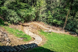 A stone pathway winding through a grassy area with dense foliage on either side. - Four Seasons Mountain Escape - Riverfront | Pet Friendly | Hot Tub (Blue Ridge)