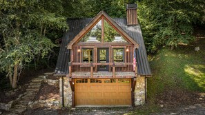 A two-story cabin with a stone foundation, a wooden deck, and a garage. - Four Seasons Mountain Escape - Riverfront | Pet Friendly | Hot Tub (Blue Ridge)