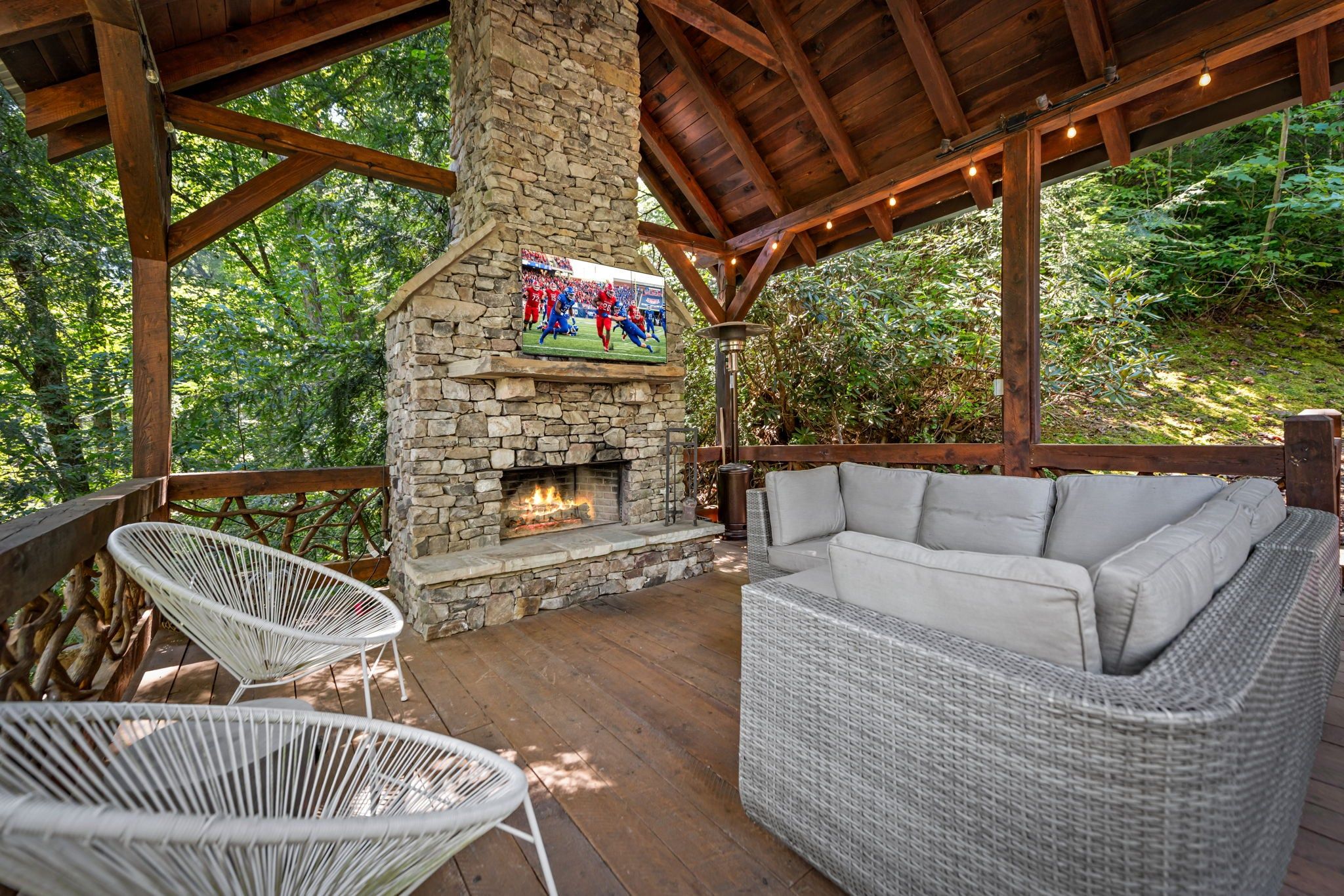 An outdoor seating area with a stone fireplace, wicker furniture, and a television screen.