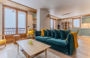 Ein gemütliches Wohnzimmer mit einem grünen Sofa, einem Holztisch und einem Essbereich mit gelben Stühlen.