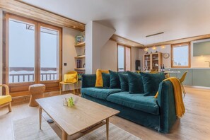 Ein gemütliches Wohnzimmer mit einem türkisblauen Sofa, einem Holztisch und einem Essbereich mit einem gelben Stuhl.