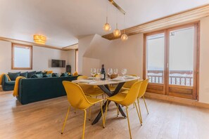Uma área de refeições com uma mesa redonda, cadeiras amarelas e uma varanda com vista.