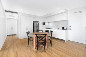 A modern kitchen with white cabinets, a central island, and a dining area with a wooden table and chairs. - Modern 2BR Walking Distance to Beach with Parking (Surfers Paradise)