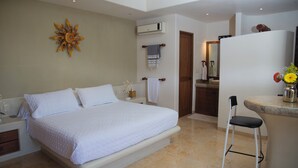 Un dormitorio con una cama grande, un escritorio pequeño con una silla, un baño con un lavamanos y un elemento decorativo en la pared.