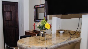 Una cocina con encimera de granito, una silla negra, un jarrón con flores y un televisor de pantalla plana montado sobre la encimera.