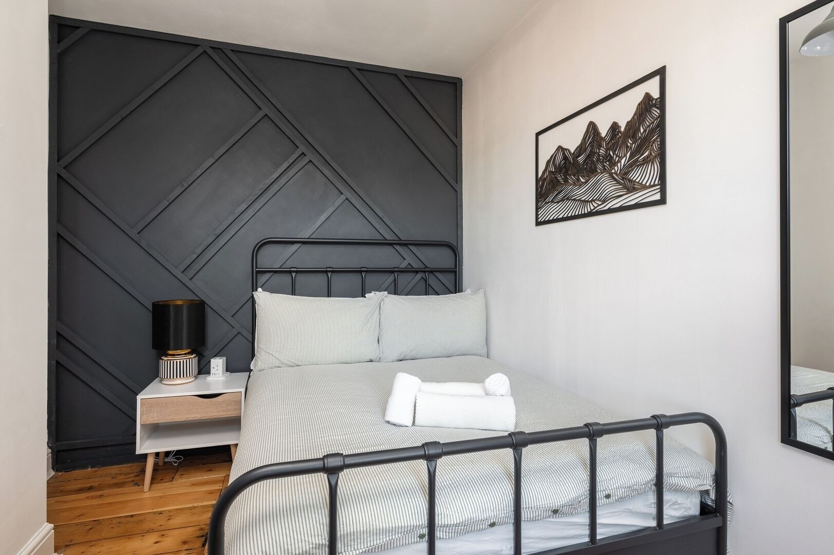 A neatly arranged bedroom with a bed, bedside table, lamp, and a framed artwork on the wall.