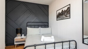 Un dormitorio ordenado con cama, mesita de noche, lámpara y una obra de arte enmarcada en la pared.