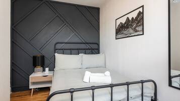 A neatly arranged bedroom with a bed, bedside table, lamp, and a framed artwork on the wall.