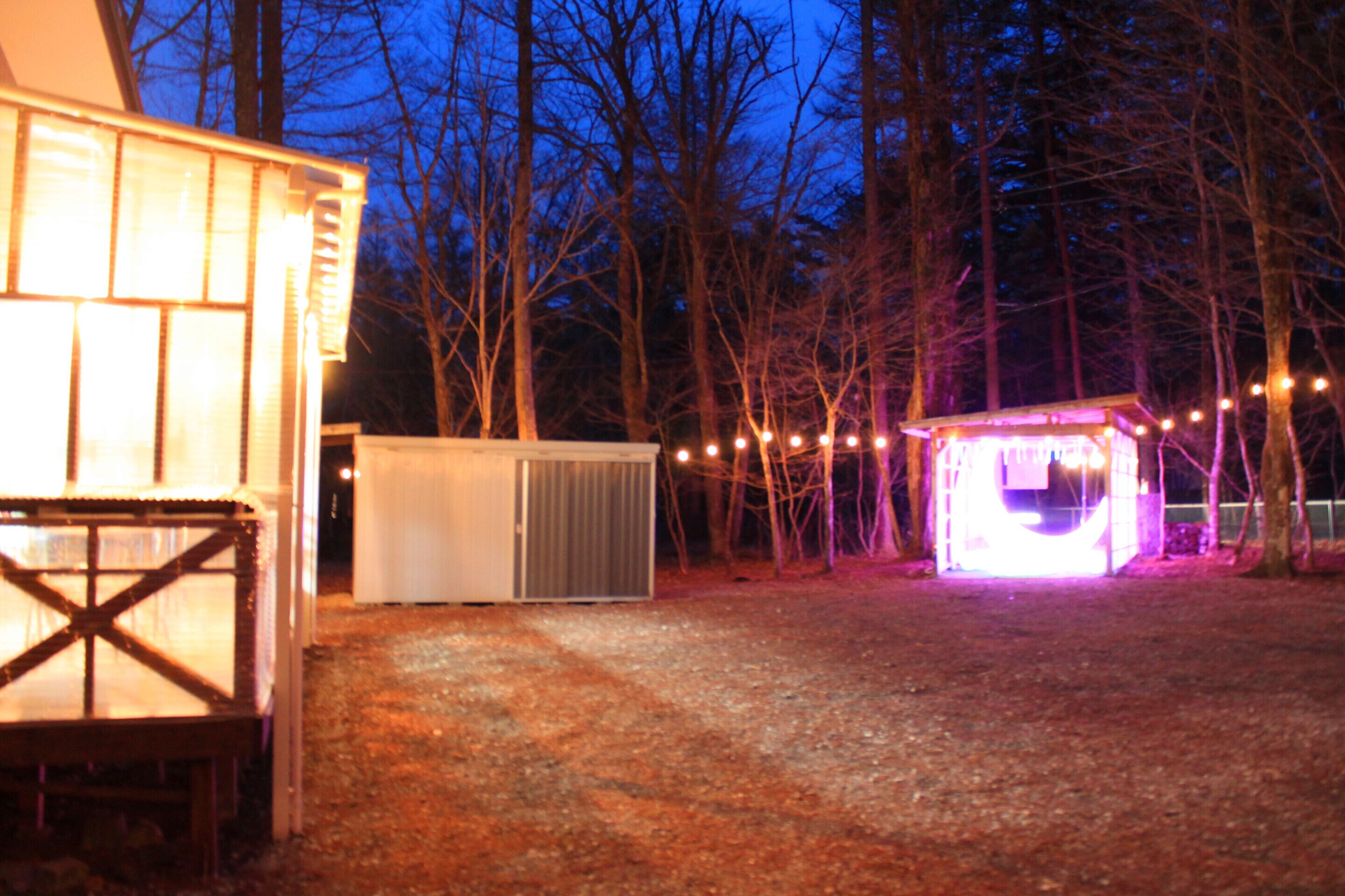 A building with a covered outdoor area, a small shed, and a string of lights.