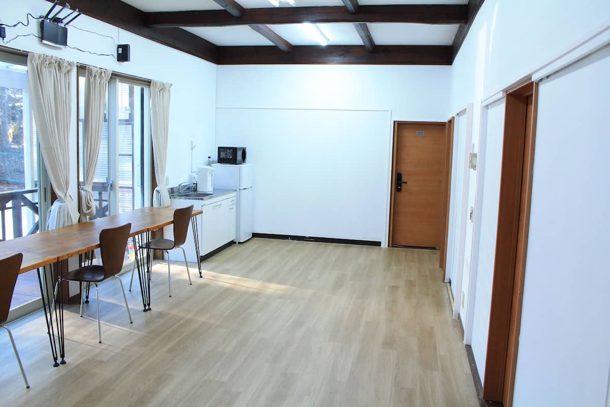 A room with a wooden dining table, chairs, a microwave, and a refrigerator.