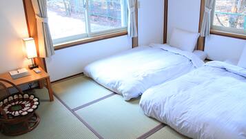 A room with two beds, a desk with a lamp, and a view of the outdoors through the window.