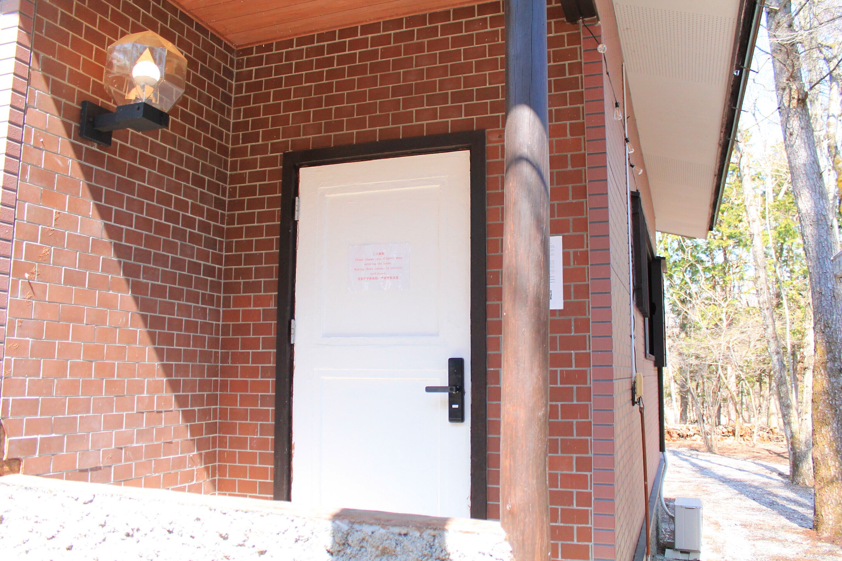 A brick building with a white door, a light fixture above the door, and a utility box to the right.
