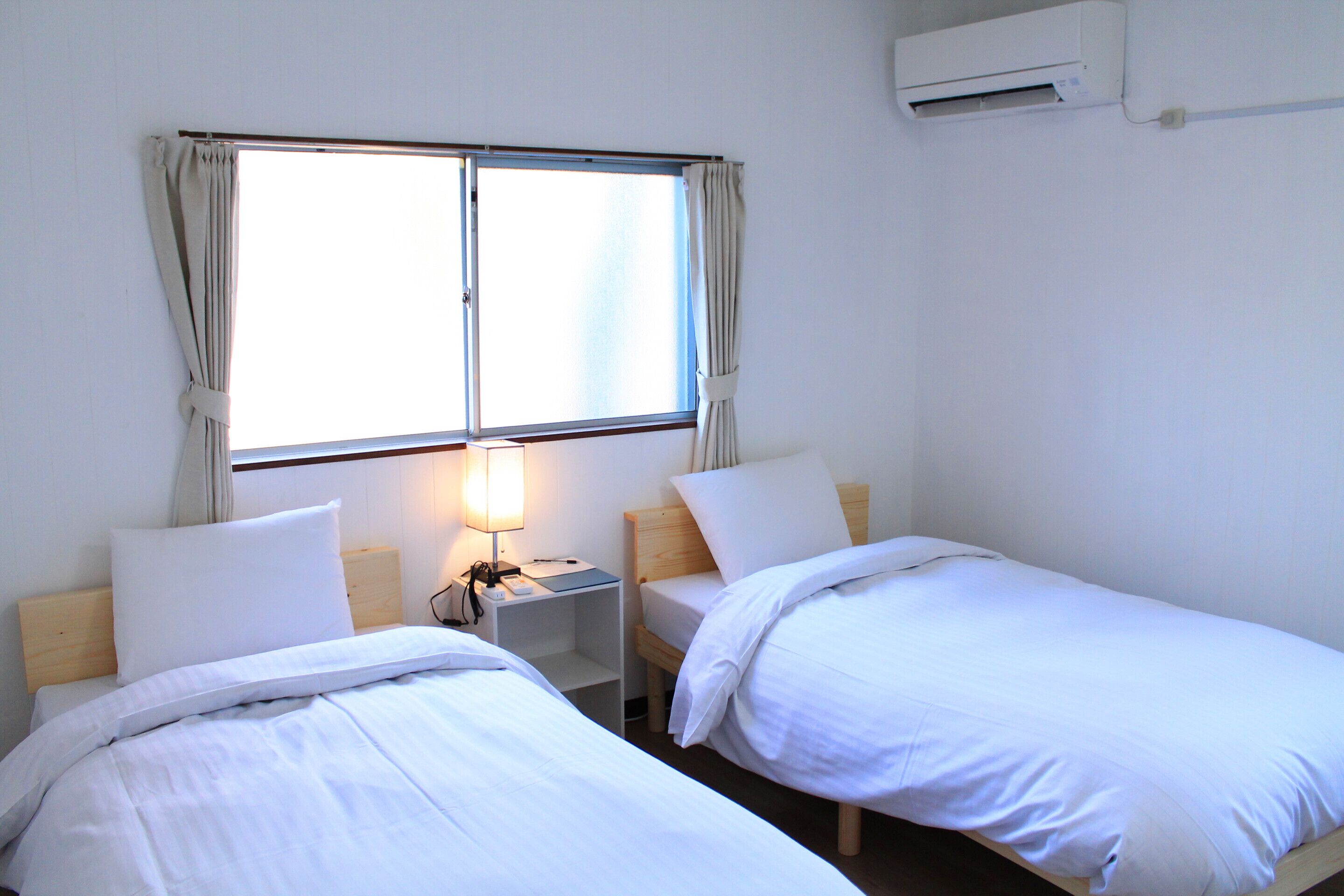 Una habitación de hotel con dos camas individuales, una mesita de noche con lámpara y una ventana con cortinas.