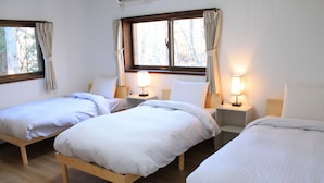 Ein Zimmer mit drei hölzernen Betten, die nebeneinander stehen, jeweils mit Nachttisch und Lampe.