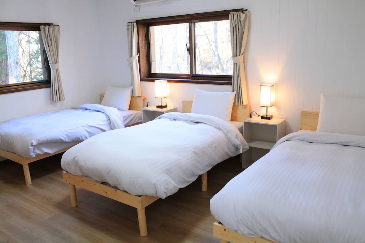 A room with three wooden beds arranged in a row, each with a bedside table and a lamp.