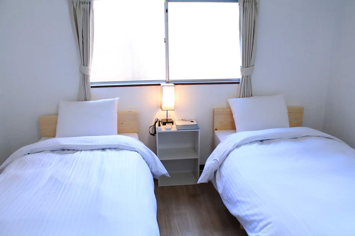 A twin room with two beds, a bedside table with a lamp, and a window with curtains.