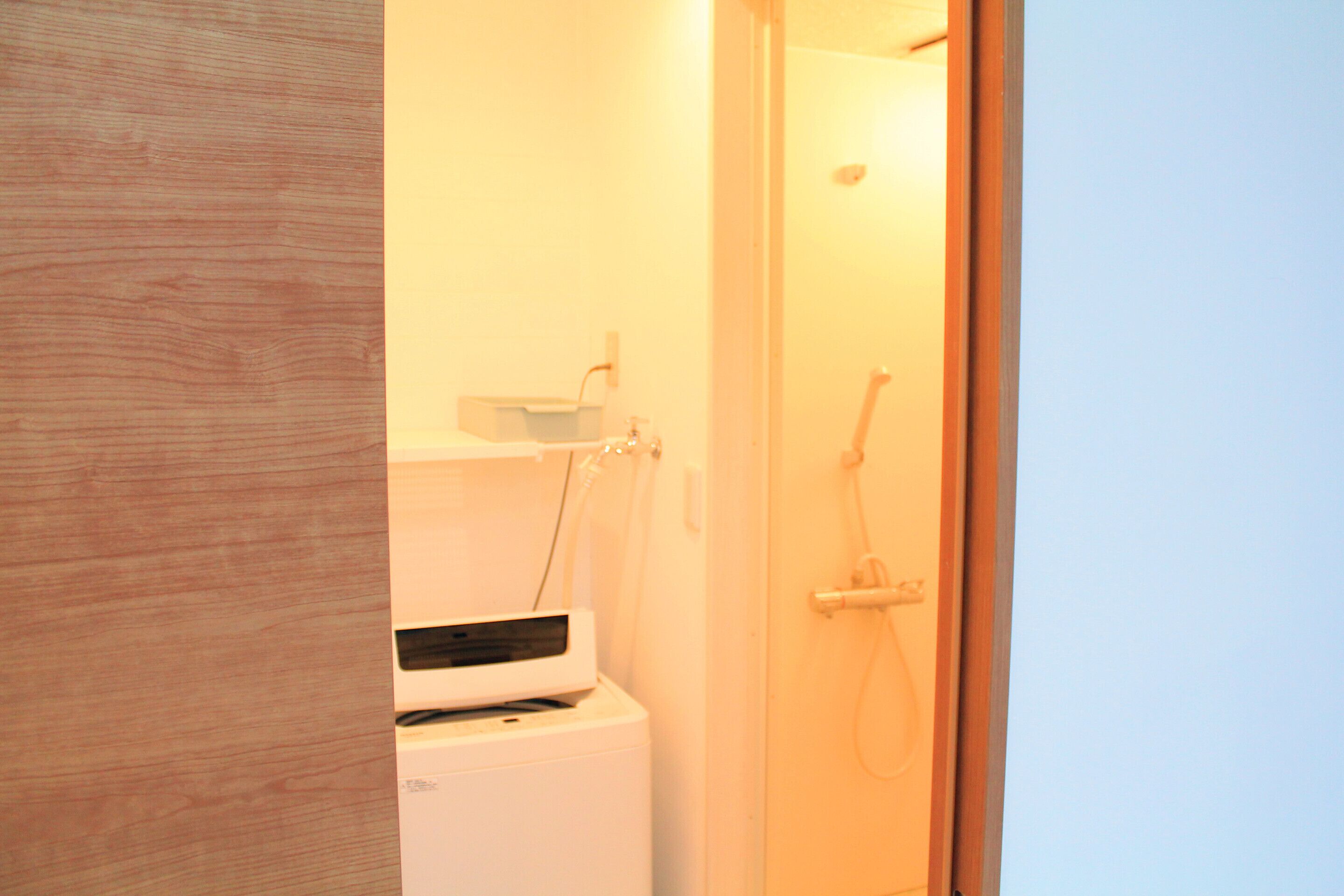 A bathroom with a white washing machine, a shelf with toiletries, and a shower area.