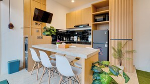 A modern kitchen with wooden cabinets, a built-in oven, a refrigerator, and a dining area with white chairs. - Villa D'Bonzai - Nusa Dua (Nusa Dua)