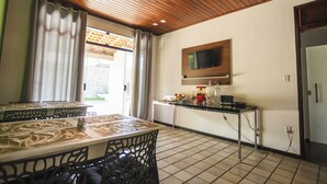 Un coin repas avec une table dressée pour deux personnes, un comptoir de cuisine équipé d’appareils électroménagers et un téléviseur fixé au mur.