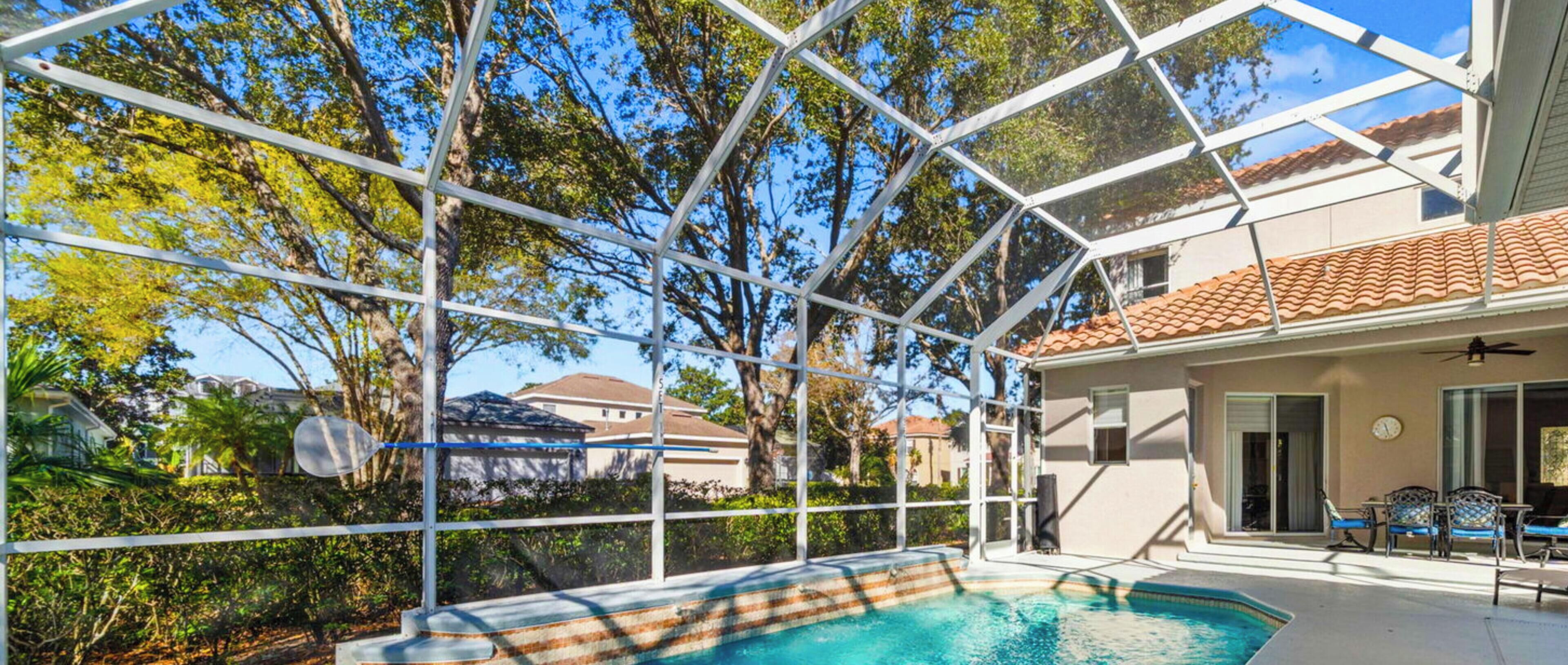 A swimming pool with a glass enclosure, surrounded by trees and a building with a tiled roof.