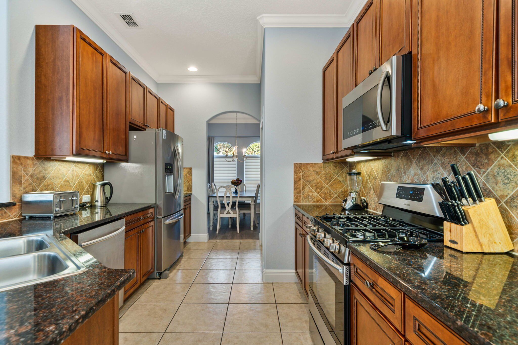 A kitchen with wooden cabinets, stainless steel appliances, a granite countertop, and a dining area with a table and chairs.