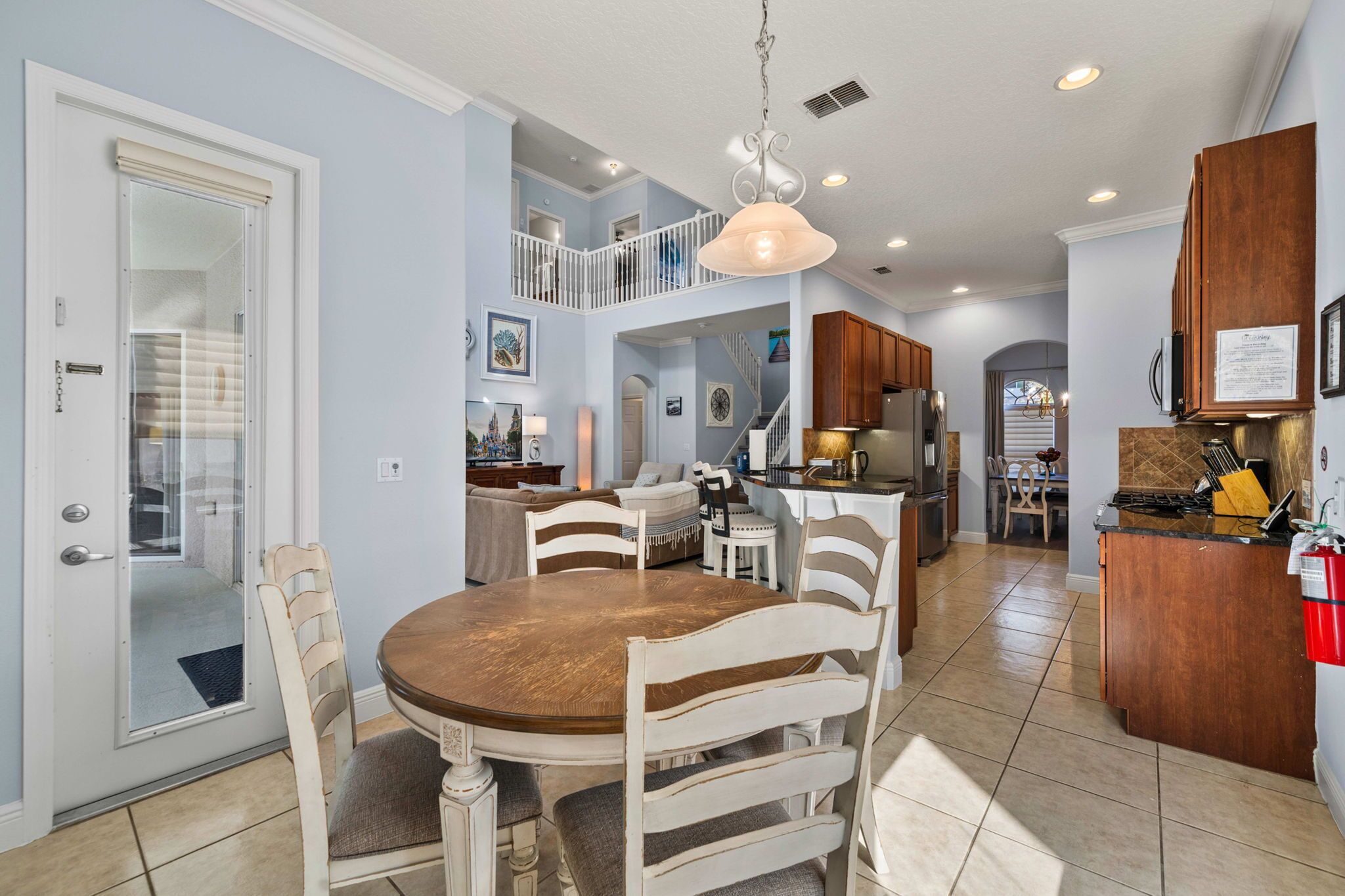 A spacious kitchen with a central island, a dining area with a round table and chairs, and a staircase leading to an upper level.
