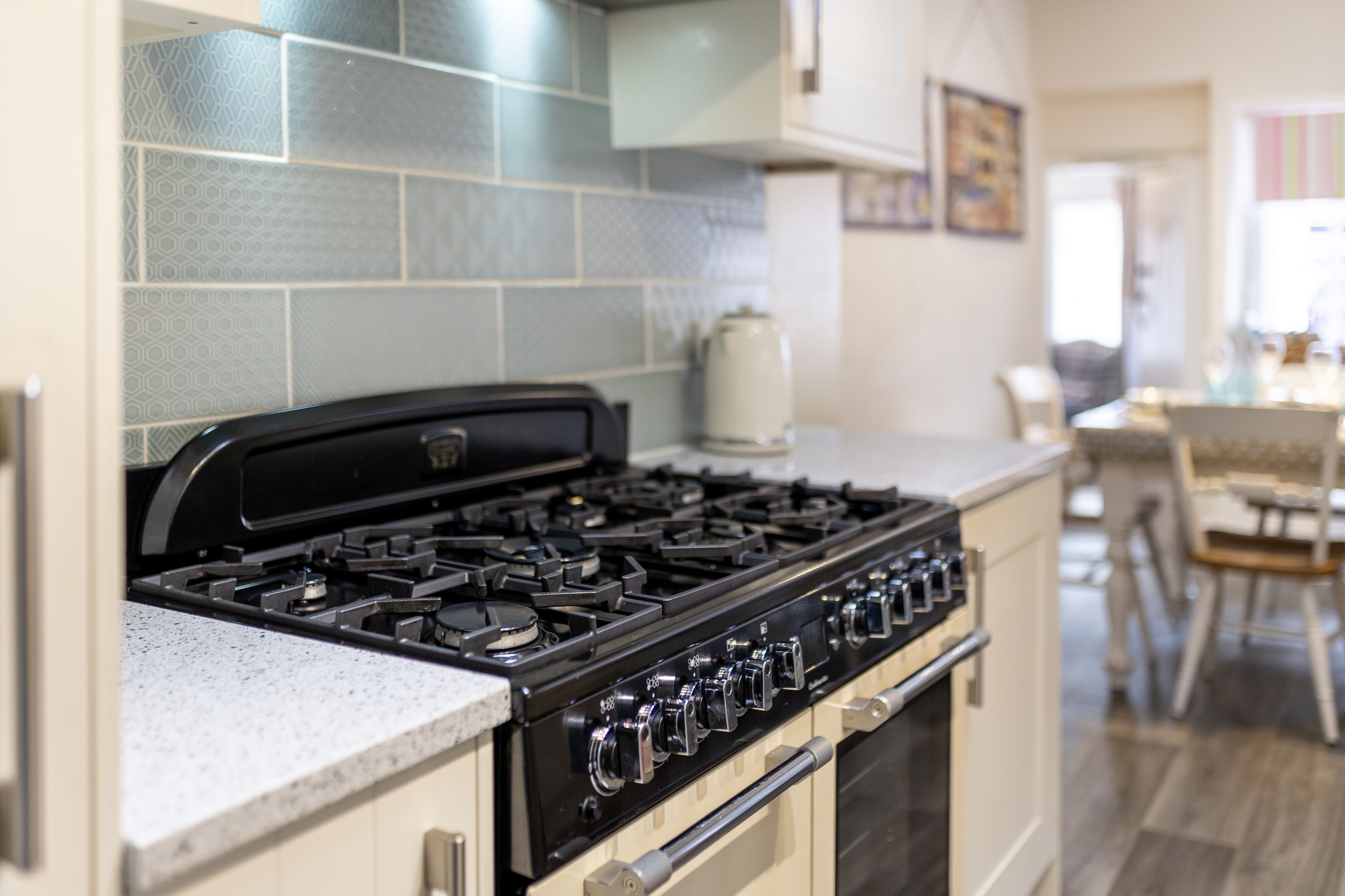 A kitchen with a gas stove, a coffee maker, and a dining area with chairs and a table.