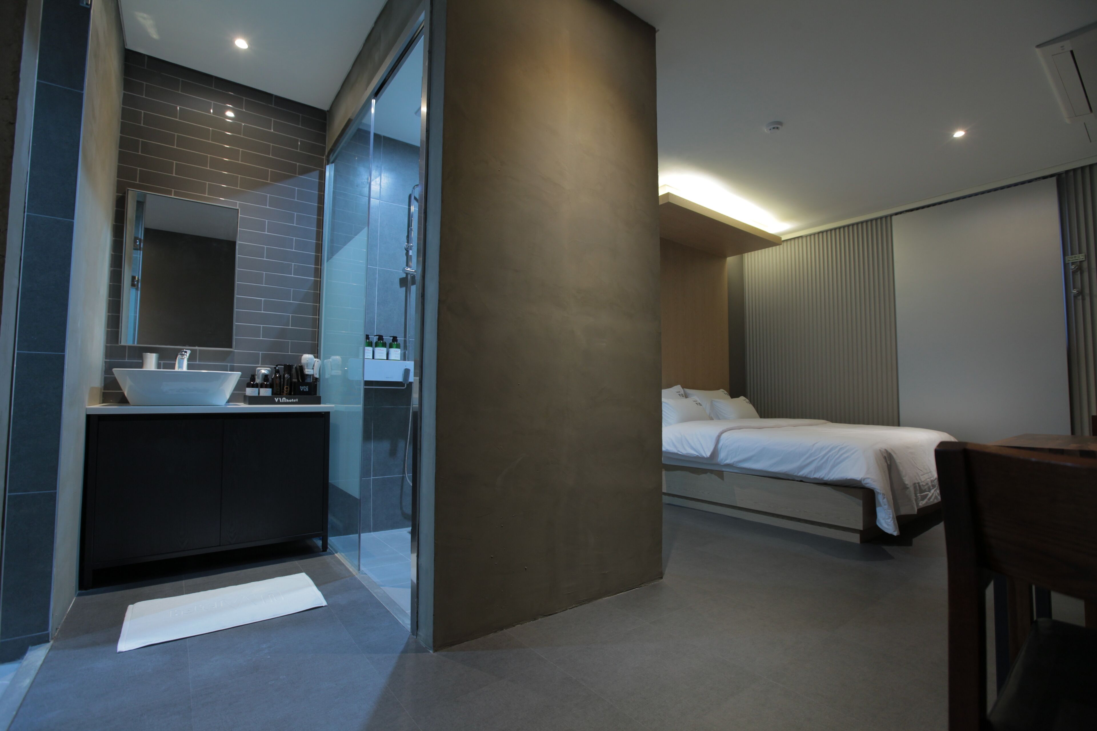 A modern hotel room with a large bed, a separate bathroom with a glass shower, and a minimalist design.