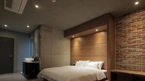 A modern bedroom with a large bed, a bedside table, a built-in bench, a brick accent wall, and a concrete wall. - Hotel Vin (Changwon)