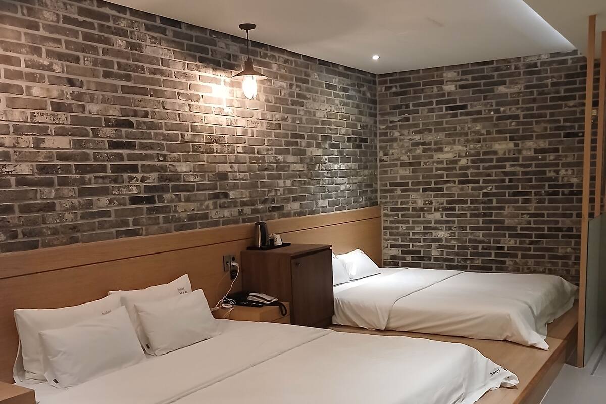 Une chambre d’hôtel avec deux lits, un mur en briques et une tête de lit en bois.