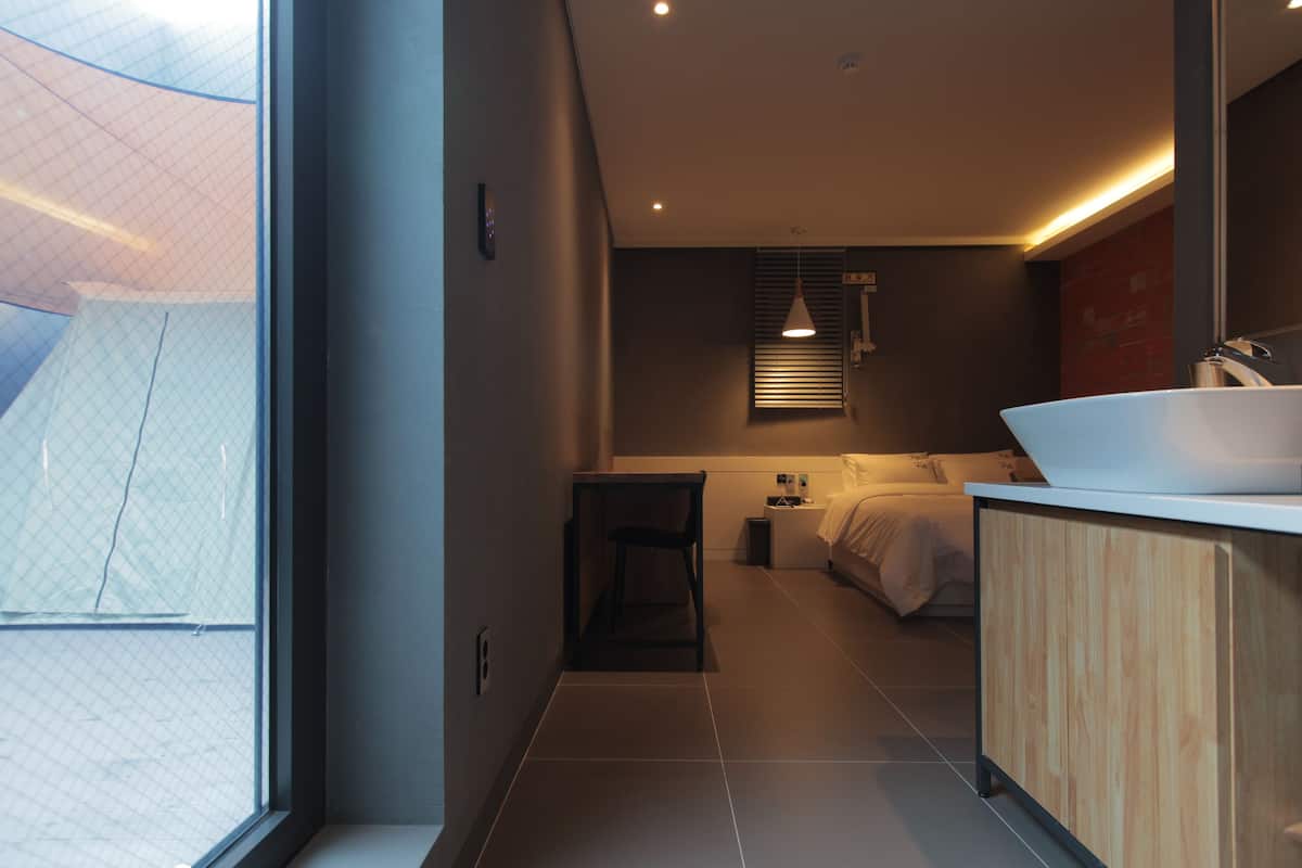 Une chambre d’hôtel moderne avec une grande fenêtre, une coiffeuse en bois, un lit et une petite table.