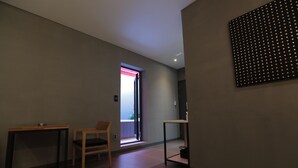 Ett modernt hotellrum med en minimalistisk design, inrett med en trästol, ett litet bord och en väggmonterad lampa.