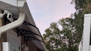 Ein überdachter Außenbereich mit Fliesenboden, einer weißen Tür und einer Klimaanlage.