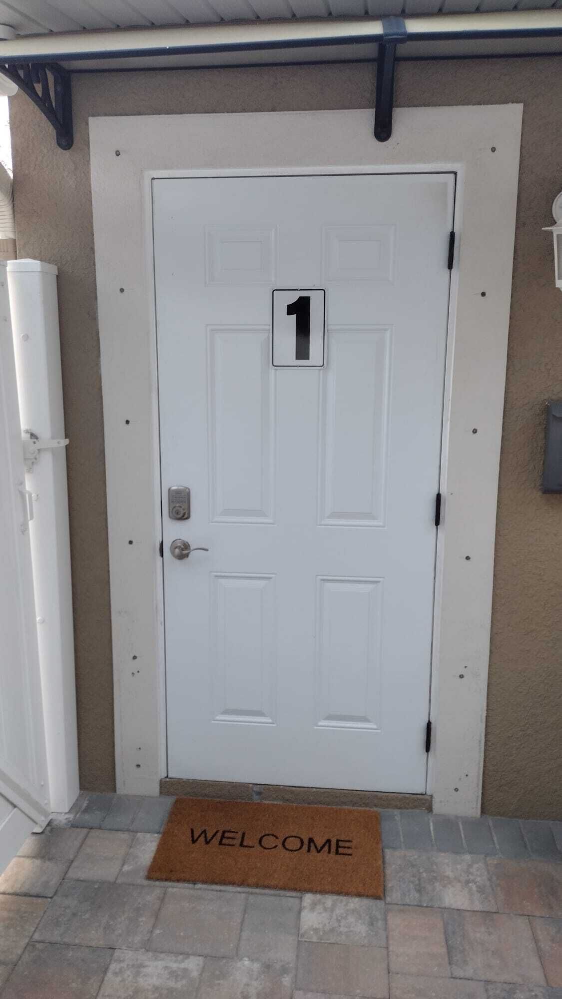 A white door with the number 1, a doormat with 'WELCOME', and a beige wall.