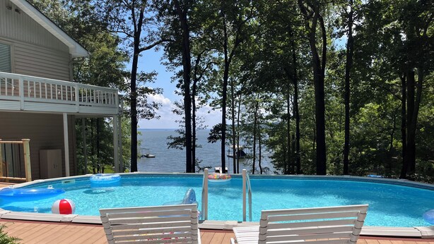 Una piscina con dos sillas reclinables blancas, una terraza de madera y vistas al mar.