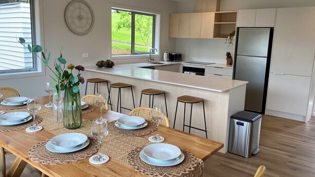 Une cuisine moderne dotée d’un îlot central, de tabourets de bar et d’une table à manger pouvant accueillir six personnes.