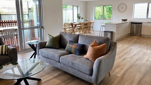 Un salon moderne avec un canapé gris, une table basse en verre et un coin repas à l’arrière-plan.