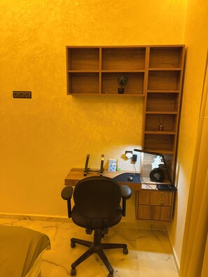 A corner office with a desk, chair, shelves, and a small plant.