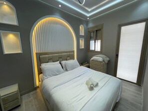 Un dormitorio moderno con cama, mesitas de noche, un espejo y una ventana con persianas.