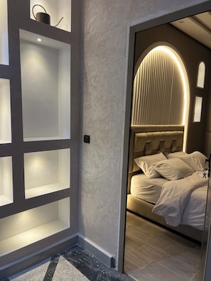 A bedroom with a bed, a built-in shelf unit, and a door leading to another room.
