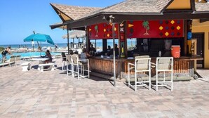 Eine Strandbar mit Außenbestuhlung und einem Pool im Hintergrund.