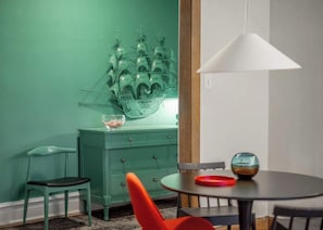 A room with teal walls, a green dresser, a round table with a red bowl, and a white pendant light. - The Codfather at Wrigley (Chicago)
