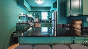 A modern kitchen with teal cabinetry, a central island, and stainless steel appliances. - The Ivy Flat | Designer 4BR Steps to Wrigley Field (Chicago)