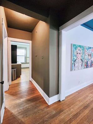 A hallway with wooden flooring, a grey wall, and a door leading to a room with a window. - Keepin’ it Golden at Wrigley (Chicago)