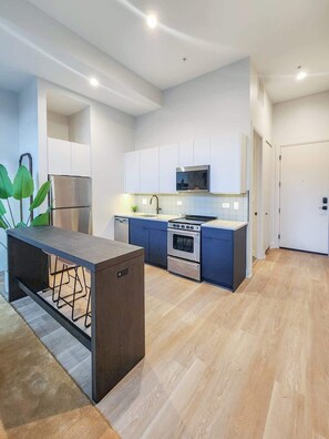 A modern kitchen with white cabinets, a stainless steel refrigerator, a microwave, an oven, and a sink. - The Avery – Boutique Bucktown/WP Studio by Transit (Chicago)