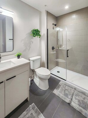 A modern bathroom with a toilet, sink, and glass-enclosed shower. - The Avery – Boutique Bucktown/WP Studio by Transit (Chicago)